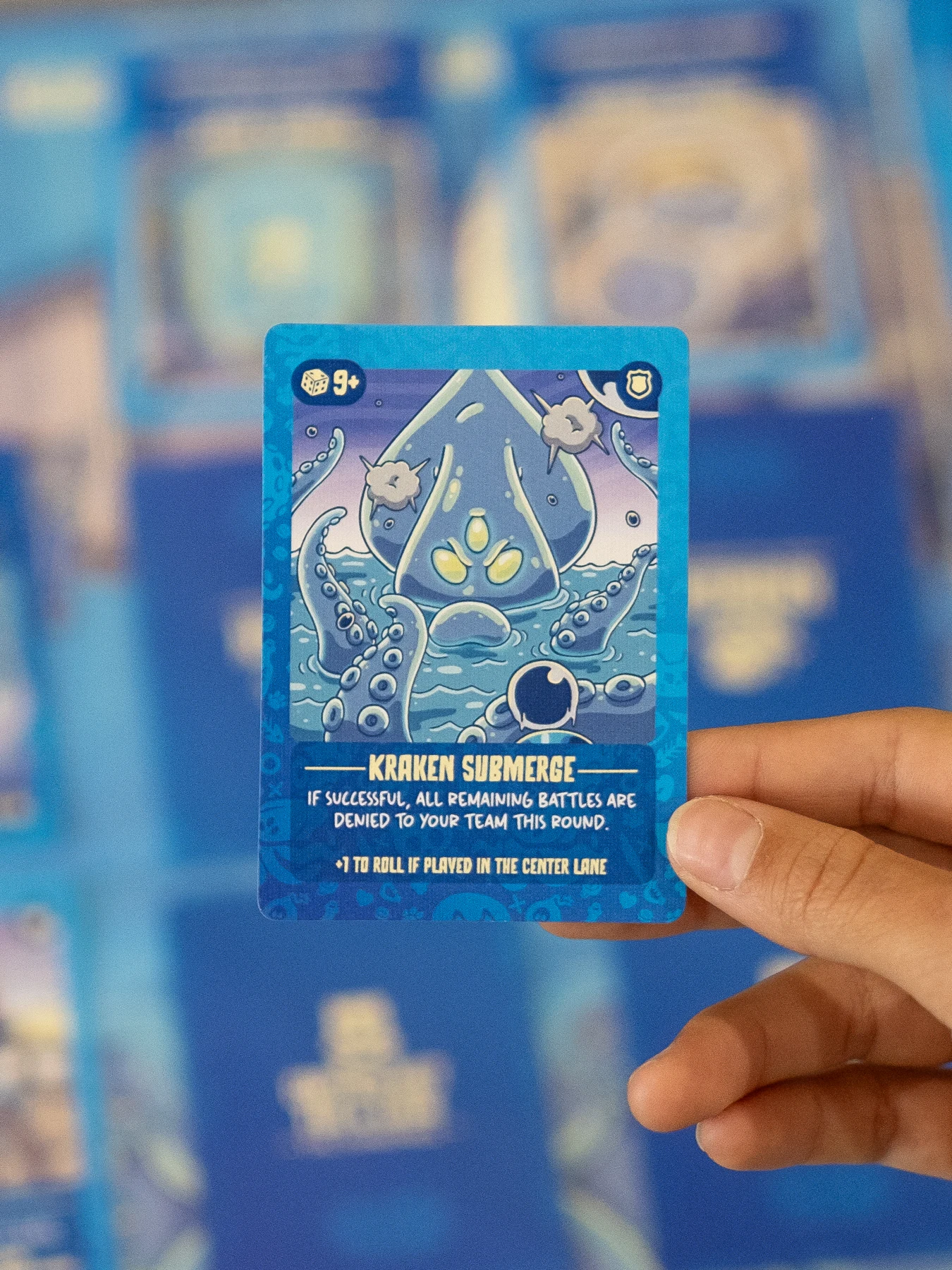 Real portrait photograph of a hand holding Kraken Submerge card with blurred game on table
