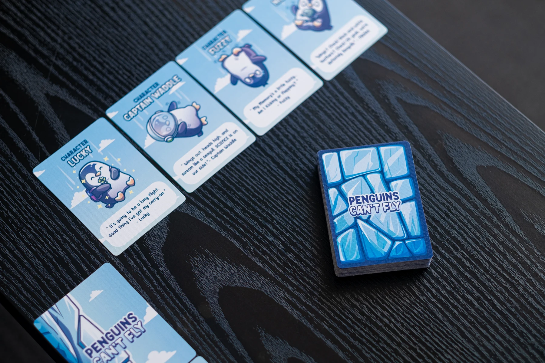 Real tabletop photograph: Penguins card layout and blue deck, dark wood table